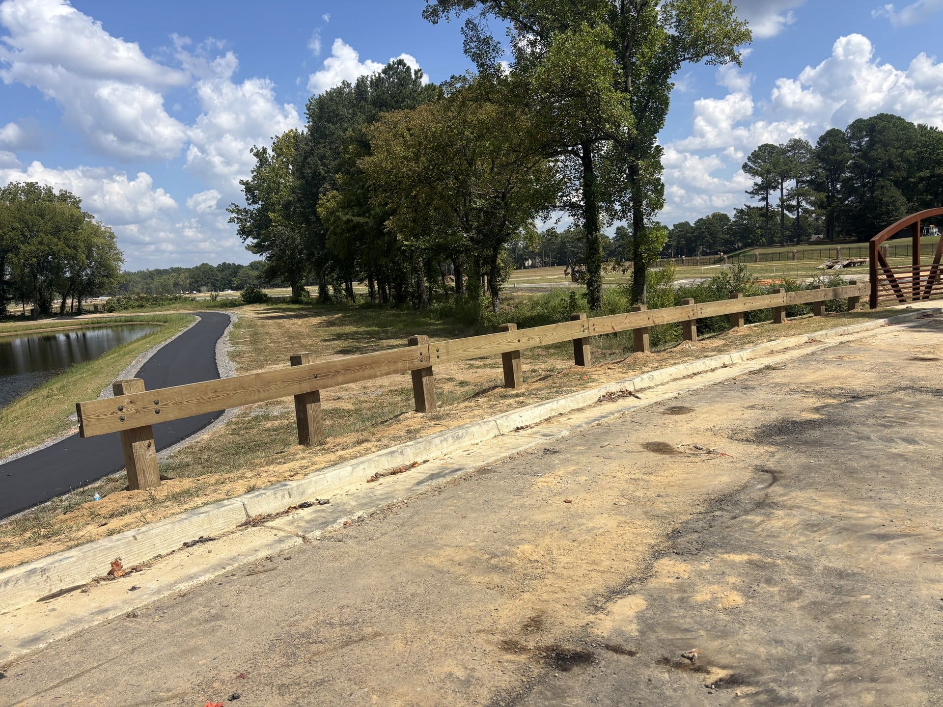 Timber guardrail installed along a greenway path and pond at a community park