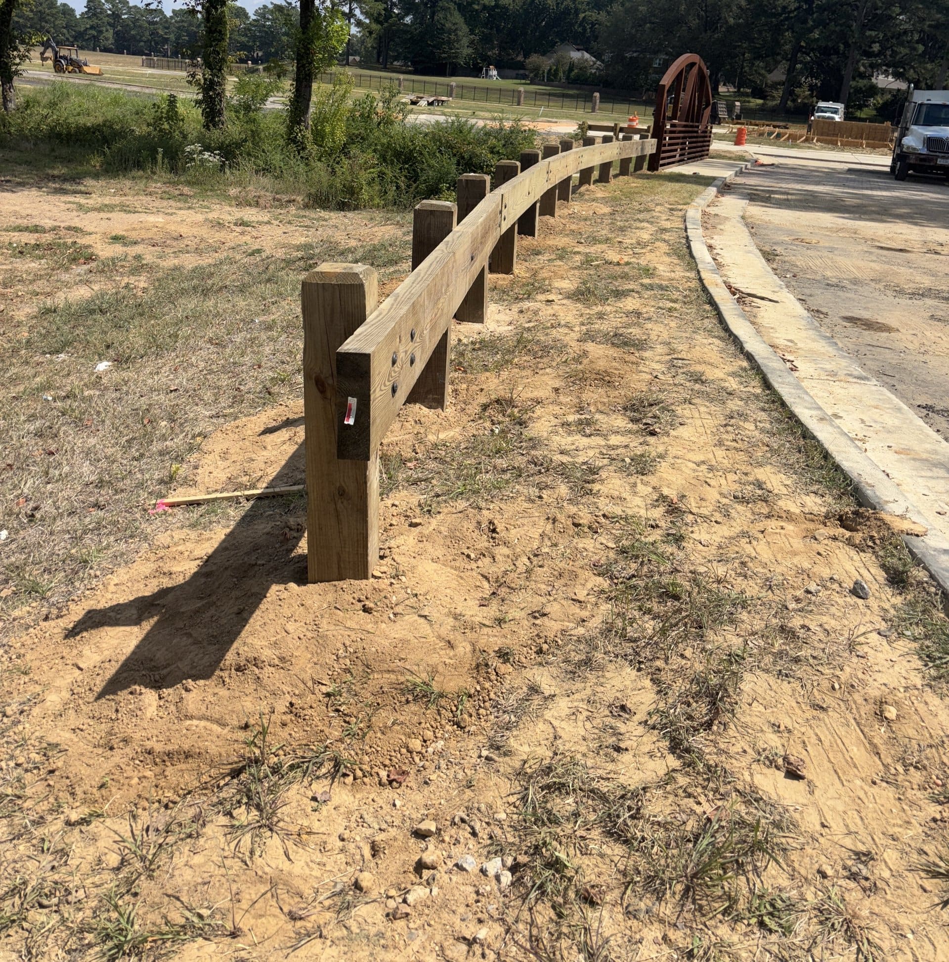 Wood post-and-rail guardrail curving toward a timber pedestrian bridge
