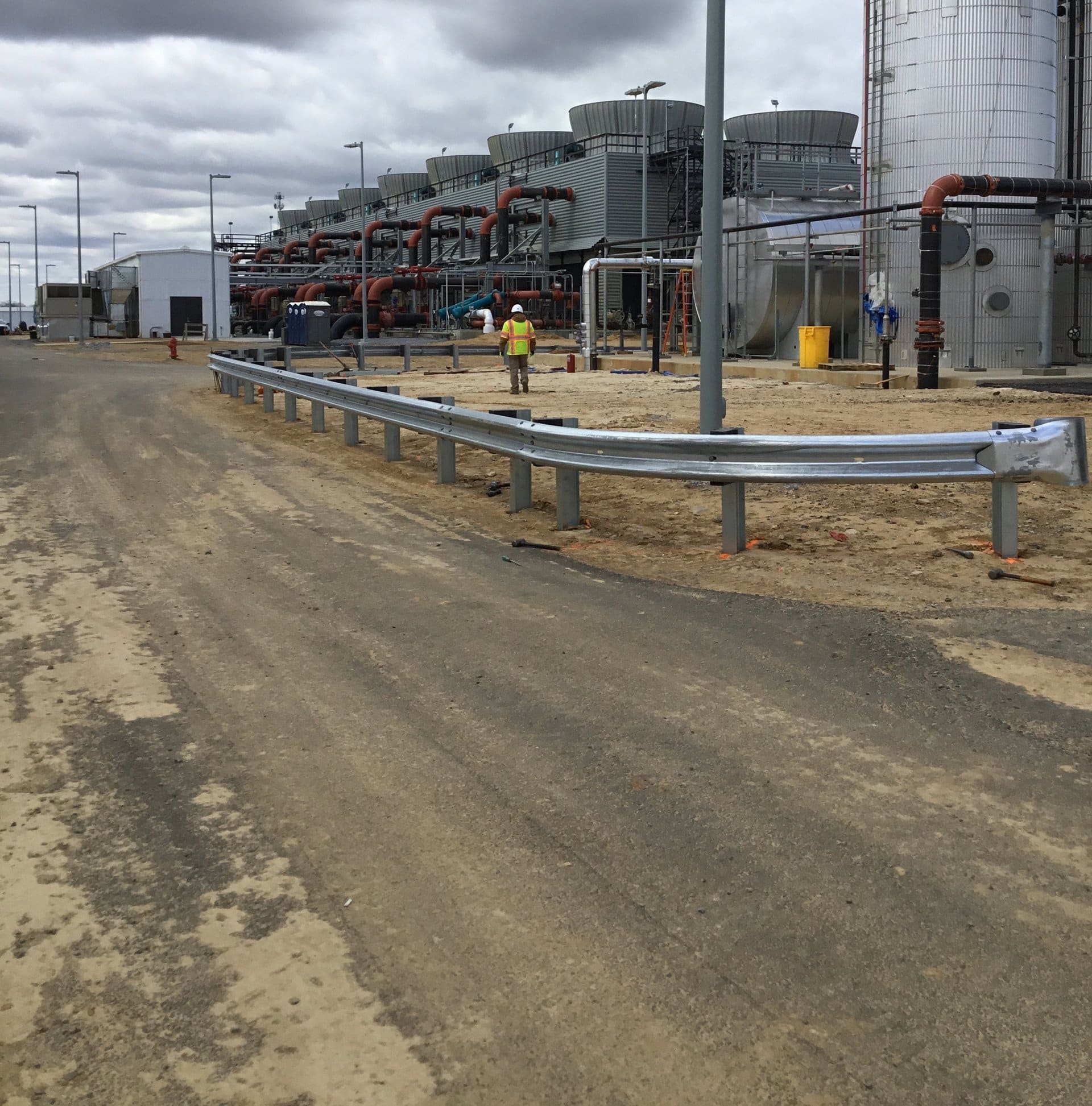 Crew member walking a fresh W-beam guardrail line at an industrial facility
