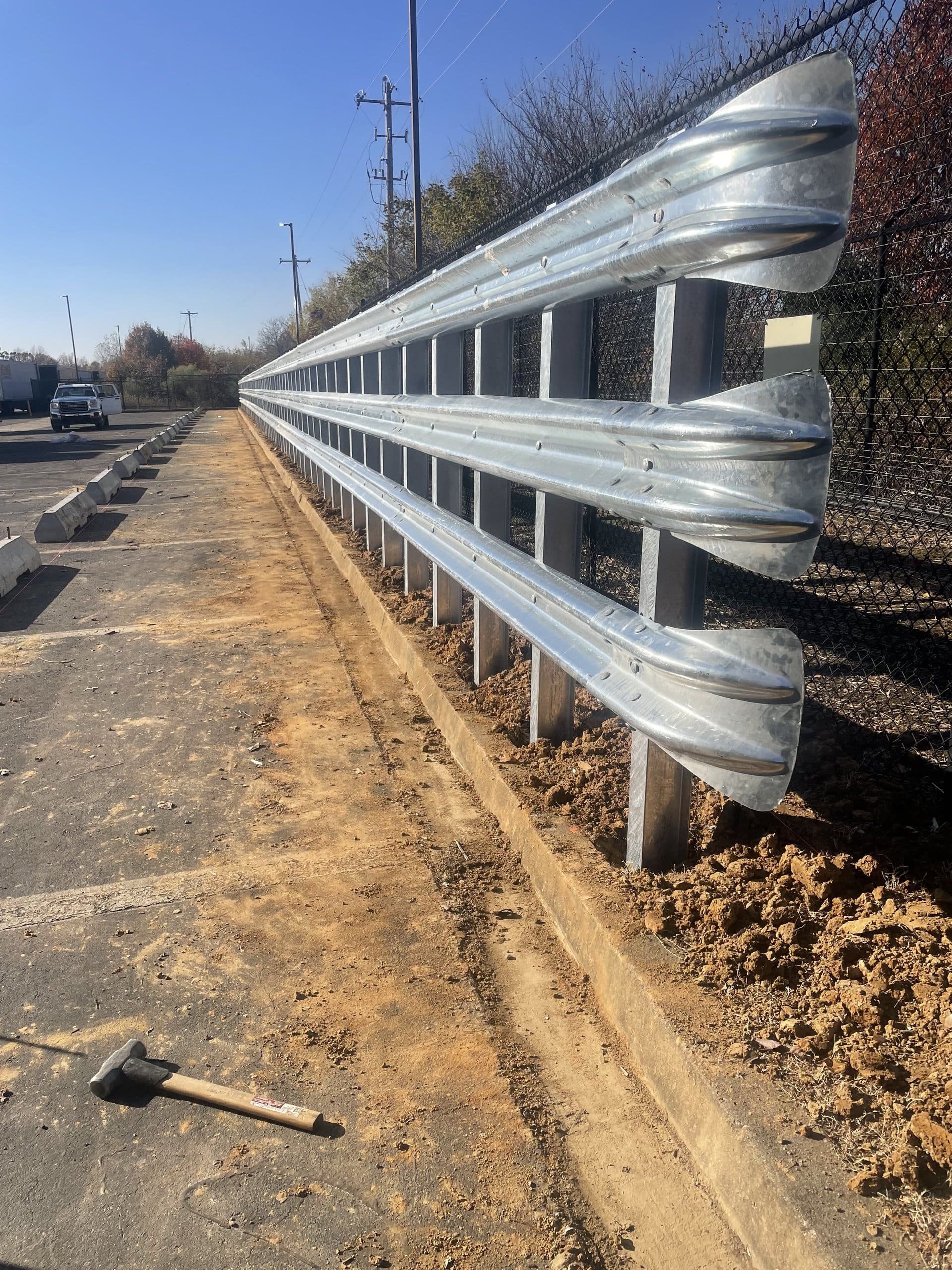 Three-high W-beam guardrail wall on steel posts protecting a commercial lot